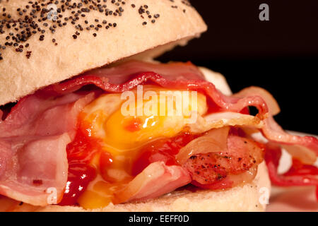 A close-up photograph of a Bacon and egg roll with tomato sauce with a black background. Stock Photo