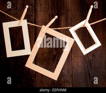 Close up of three photo frames and clothes pegs on a rope over a wooden background. Stock Photo