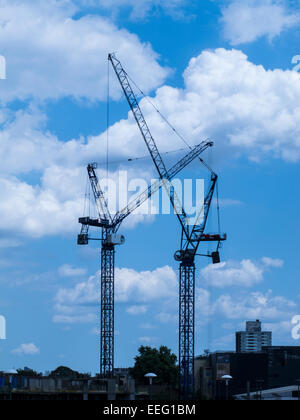 Cranes in a construction site silhouetted against blue skies and white clouds Stock Photo