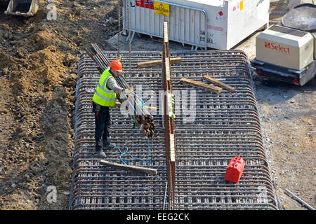 Steelfixer guiding a crane lowering bundle of reinforcing rods onto steel foundation frame Heygate Estate Southwark South London England UK Stock Photo