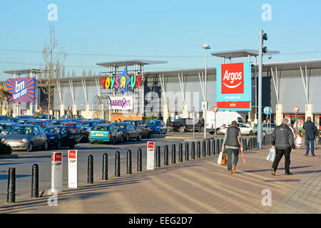 Back view shoppers with shopping bags walking towards Argos B&M retail business store units & car parking at the Landsec Lakeside retail park Essex UK Stock Photo