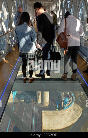 Visitors and tourists standing on glass floor on Tower Bridge high level walkway with bridge & road traffic and river thames below London England UK Stock Photo