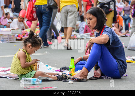 Intramuros, Manila, Philippines, 16th Jan 2015. Woman vendor feeds her daughter while taking a break selling Papal souvenir items in a street near Manila Cathedral, Intramuros on Friday, January 16, 2015 where the Holy Father was scheduled to celebrate Holy Mass with the country's bishops, priests, and other religious during his Apostolic Visit to the Philippines. Stock Photo