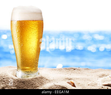 Photo of cold beer botle in the sand. Sparkling sea at the background. Stock Photo