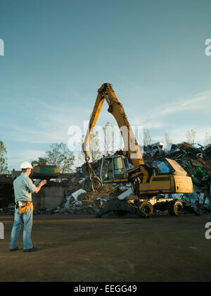caucasian engineer wearing protective equipment, holding digital tablet and looking at scrap metal pile Stock Photo