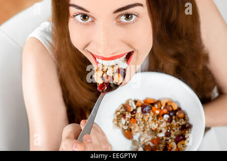 Young positive woman eating granola breakfast on the couch at home. Up-view Stock Photo