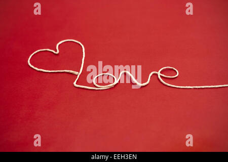 Love word and heart symbol made of white twine on red background for your Valentine or Mother Stock Photo