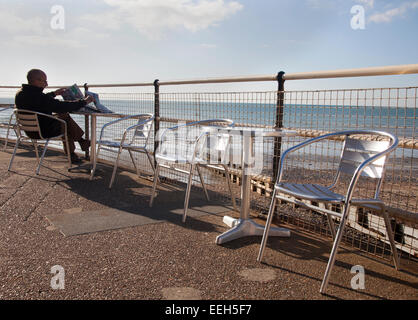 Man sitting and reading newspaper on promenade at landward end of Worthing pier, Worthing, West Sussex , England. Stock Photo