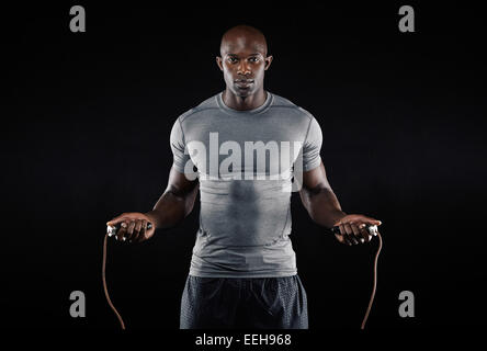 Masculine man skipping rope in dark. Portrait of muscular young man exercising with jumping rope on black background Stock Photo
