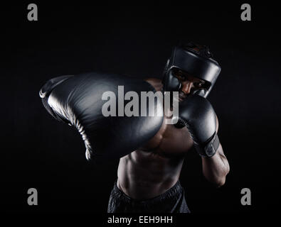 Portrait of African male practicing boxing against black background. Male boxer throwing a punch in front. Young sportsman. Stock Photo