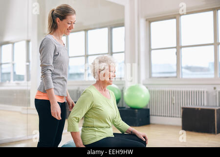 Portrait of female instructor assisting senior woman exercising in gym. Two fitness woman at health club exercising. Stock Photo