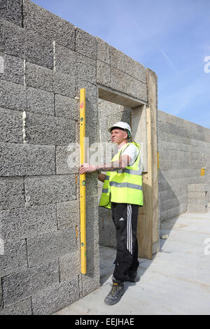 A workman uses a level to check the straightness of Durisol cement-bonded wood fibre blocks whilst building an apartment block. Stock Photo