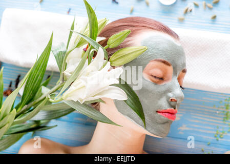 Young woman with spa facial mask on her face lying on blue table with flower, candles and sea salt in the beaty salon Stock Photo