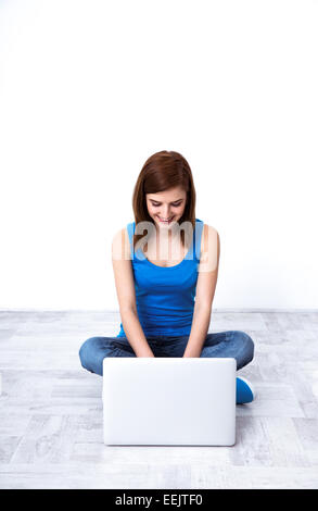 Happy woman sitting on the wooden floor and typing on the laptop Stock Photo