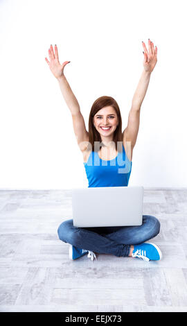 Cheerful woman sitting at the floor with laptop and raised hands up Stock Photo