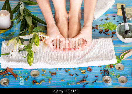Woman taking care of her legs on the bath towel in spa with flower, candles and herbs on blue wooden desk Stock Photo