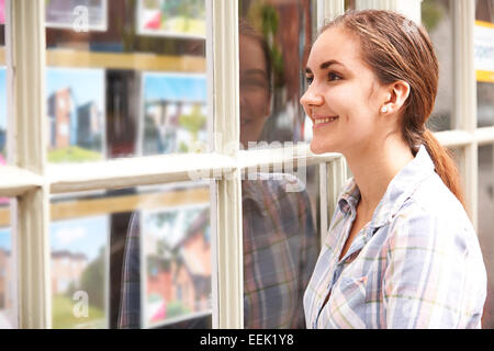 Smiling Young Woman Looking In Window Of Estate Agents Stock Photo