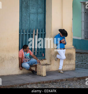 Two men on a street corner in Trinidad, Cuba. One seated and one standing with hat on. Stock Photo