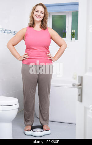 Happy Woman Weighing Herself On Scales In Bathroom Stock Photo