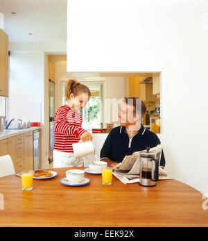 Father and daughter having breakfast together, in kitchen, bonding, laughing while daughter pours milk onto her father's cereal Stock Photo