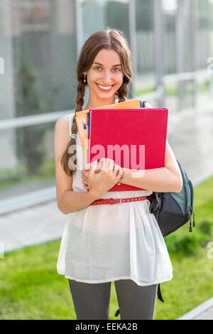 Student girl outdoors with backpack and books going to school and smiling Stock Photo