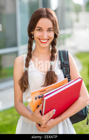 Student girl outdoors with backpack and books going to school and smiling Stock Photo