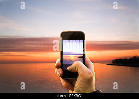 A person taking a picture of a sunset with their smartphone Stock Photo
