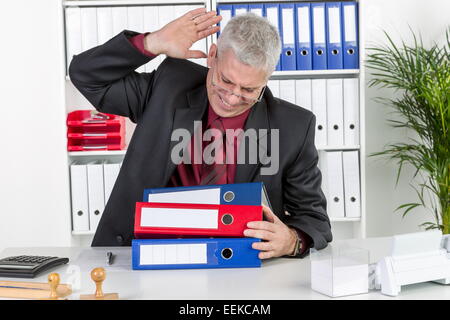 Mann mittleren Alters sitzt im Büro, ärgert sich, ist überlastet, Middle-aged man, sitting in his office, is upset and over-work