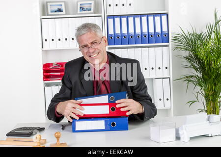 Mann mittleren Alters sitzt im Büro, ägert sich, ist überlastet, Middle-aged man, sitting in his office, is upset and over-worke