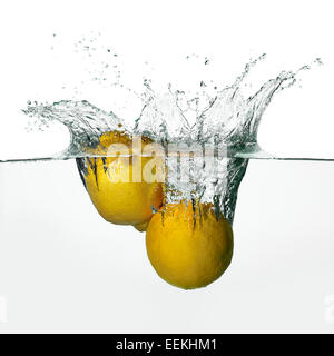 Closeup of fresh and health lemons falling into clear water with big splash isolated on white background Stock Photo