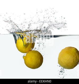 Closeup of fresh and health lemons falling into clear water with big splash isolated on white background Stock Photo