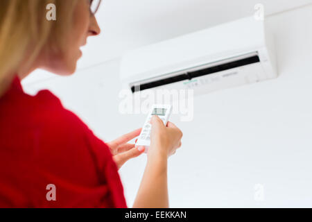 Woman using air-condition with remote control Stock Photo