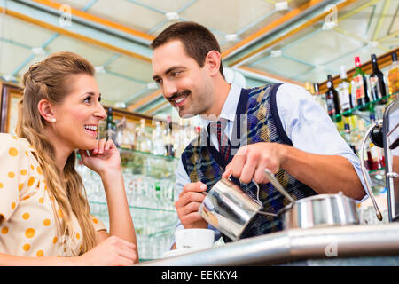 Girl in cafe or coffee bar flirting with barista who is busy preparing Cappuccino with professional machine Stock Photo