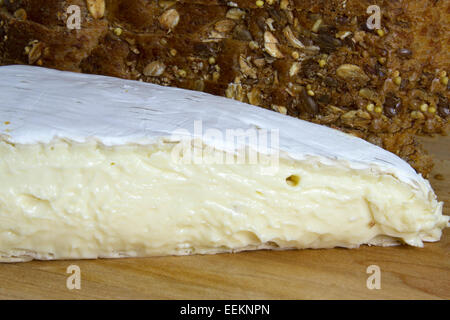 Wedge of brie cheese on wooden cutting board with loaf of whole grain bread Stock Photo