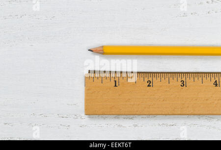Close up of a traditional wooden ruler, with metal edge, and yellow pencil on white boards Stock Photo