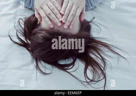 Woman lying on bed covering her eyes with hands Stock Photo