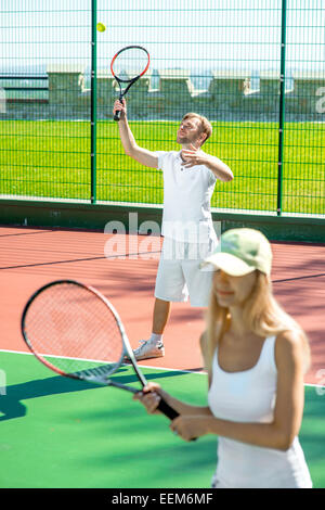 Young married couple playing tennis in white sportwear on the tennis court outside in the summer Stock Photo