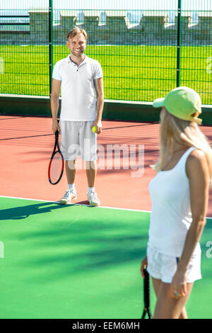 Young married couple playing tennis in white sportwear on the tennis court outside in the summer Stock Photo