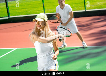 Young married couple playing tennis in white sportwear on the tennis court outside in the summer Stock Photo