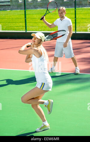 Young married couple playing tennis in white sportwear on the tennis court outside in the summer Stock Photo