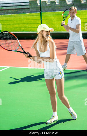 Young married couple playing tennis in white sportwear on the tennis court outside in the summer Stock Photo