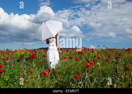 Woman with white umbrella standing in field of red poppies Stock Photo