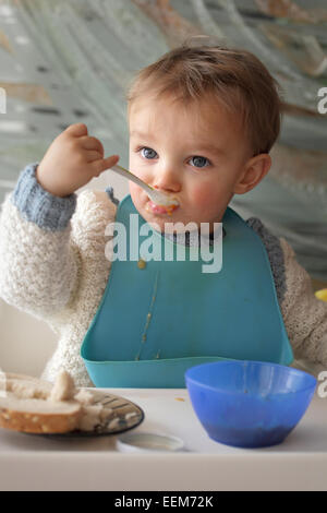 Portrait of baby boy (18-23 months) wearing baby bib eating at table Stock Photo