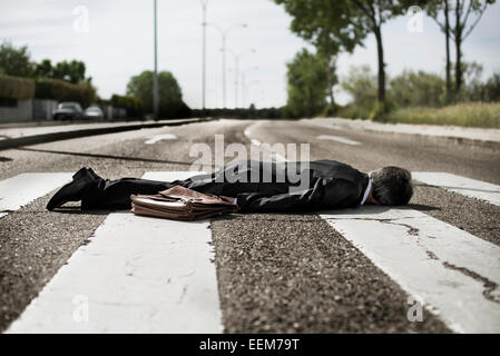 Businessman lying on a zebra crossing in the middle of the street Stock Photo
