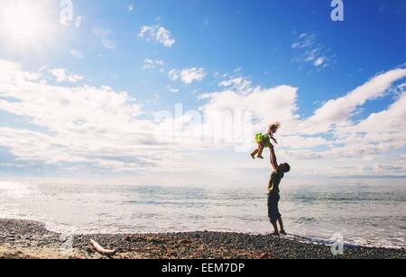Father standing on beach throwing his daughter in the air, USA