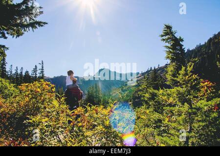 Young boy (2-3) sitting on father's shoulders looking at mountain Stock Photo