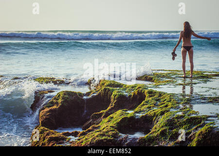 Woman standing on rocks by the sea, Bali, Indonesia Stock Photo