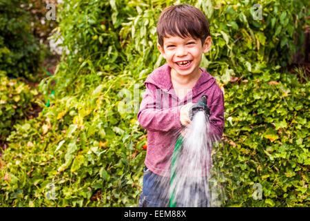 Mixed race boy playing with hose in garden Stock Photo