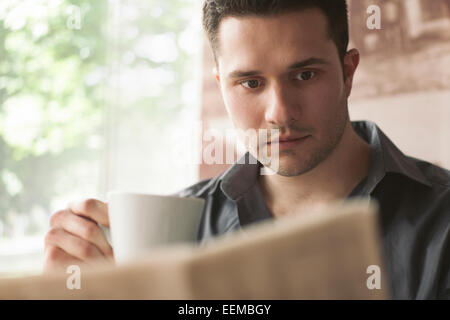Man drinking cup of coffee and reading newspaper Stock Photo