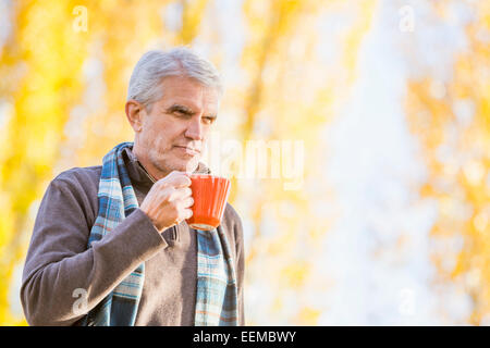 Older Caucasian man drinking coffee near autumn trees Stock Photo